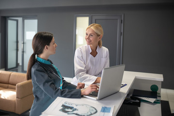 Young female intern and blond doctor sitting at the table