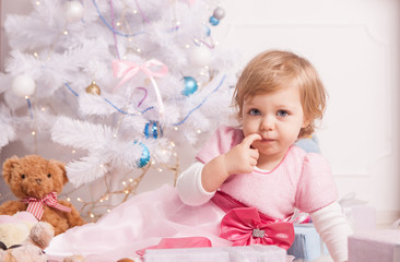 Cute little girl in an elegant dress sits on the background of a beautifully decorated Christmas tree