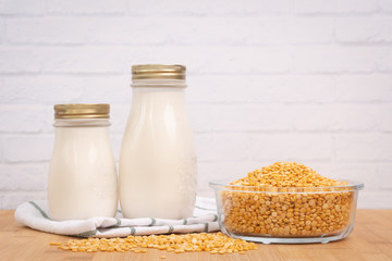 Fresh homemade oat milk in glass bottles set beside a pile of rolled oats in a bowl on the wooden kitchen table. Oat milk or plant milk are high protein and dairy-free, rich in vitamins and nutrition 