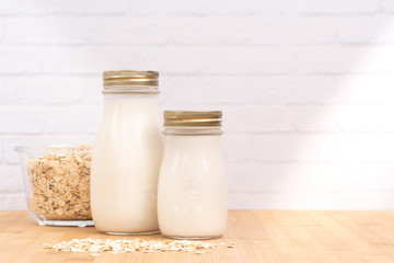Fresh homemade creamy oat milk in glass bottles and bowl of rolled oats on beautiful wooden kitchen...