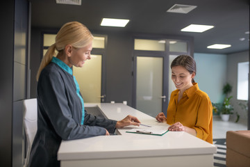 Blond woman in grey jacket talking to female visitior