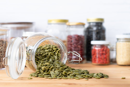 Beautiful closeup of a pile of dried pumpkin or pepita seeds pour out from a glass jar airtight container on the wooden kitchen counter. The seeds contain lots of nutrients for heart health and bones.