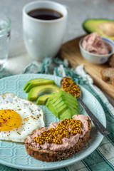 Healthy breakfast with cooked egg, chopped avocado on a plate, cereal bread with French mustard paste, a glass of water with coffee
