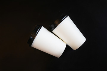 Several, two paper white cups with a plastic black lid for takeaway coffee on a black background of the table in the cafe.Close up view of disposable paper coffee Cup in cafe