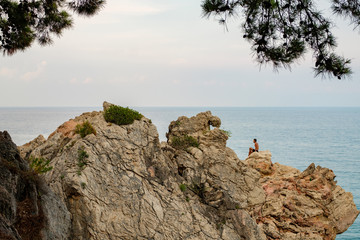 in the foreground is a rock on it sits a man the background is the sea and the sky