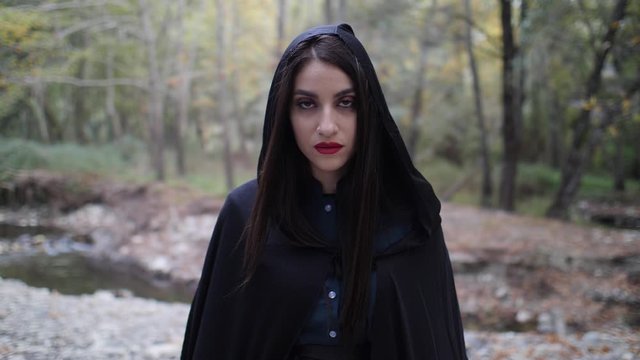 Portrait of a mysterious beautiful woman in a dark cloak as she looks up and stares deeply into the camera in slow motion.