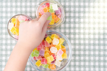 Closeup, Hand of little child take jelly / gummy cubes with sugar coated from glass bowl. Snacks...