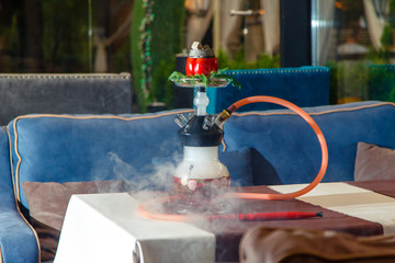 Hookah on vegetables. Hookah with a round transparent flask, which contains chopped vegetables: pepper, cucumber, radishes, herbs. Vegetables are filled with red liquor. Lots of smoke.