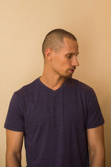 An attractive young man in a blue T-shirt poses against a beige wall.