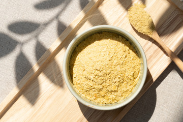 Top view & Closeup, Yellow flakes of nutritional yeast in ceramic bowl and wooden spoon, excellent source of vitamins, minerals, and high-quality protein for plant-based diet / vegan food.