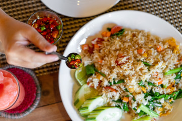 Female hand holds a spoon with seasoning of red and green pepper on a background of fried rice.