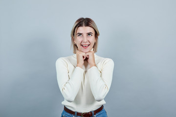 Pretty young caucasian lady keeping fists on chin with over gray background. Looks happy, funny...