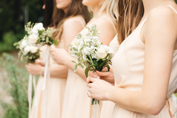 Obraz na płótnie Canvas Glorious bridesmaids in light dresses holding beautiful flowers