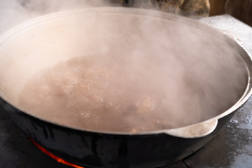 Preparation of shurpa in a cauldron on a Russian stove on an open fire.