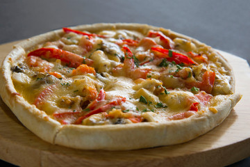 Hot pizza with tomatoes and pepper on a wooden plate.