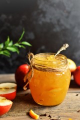 Homemade apple jam with orange zest. Jam in a glass jar on a dark background, on a wooden table. Beautiful spoon.