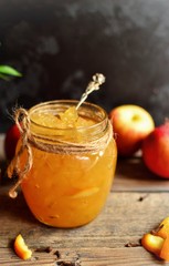 Homemade apple jam with orange zest. Jam in a glass jar on a dark background, on a wooden table. Beautiful spoon.