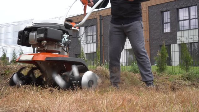Gardener loosens soil with walking tractor in urban flower beds. Gimbal movement