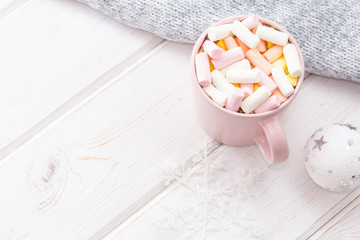 A mug of hot chocolate with marshmallows near gray wool fabric on a white wooden background