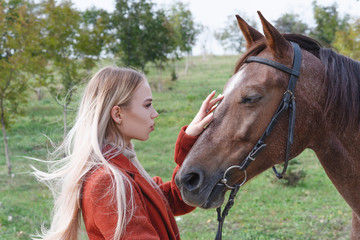 A beautiful, young, stylish girl stands next to a horse next to the road.