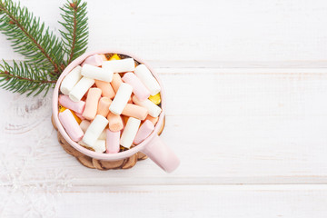 A mug of hot chocolate with marshmallows and spruce branch on a white wooden background (planks)