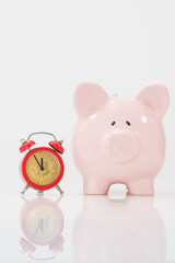 Concept image illustrating a deadline to invest in cryptocurrency showing a pink piggy bank and a red alarm clock with a bitcoin as the clock face.  