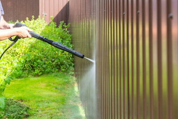 Cleaning fence with high pressure power washer, cleaning dirty wall.