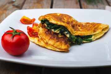 Traditional omelet with vegetables, spinach, tomatoes and herbs on a wooden table in a restaurant.
