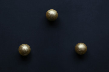 Flat lay: three gold sparkling Christmas toy balls on a dark blue background for New Year tree decoration.