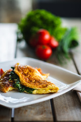Traditional omelet with vegetables, spinach, tomatoes and herbs on a wooden table in a restaurant.