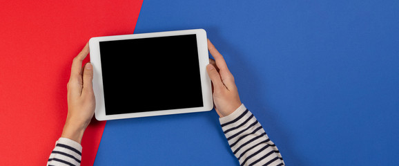 Female hands with tablet computer on blue and red background. Top view