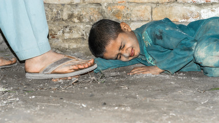 a homeless an Asian child is sleeping on the ground in a cold weather cause of poverty and wearing...