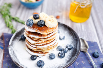 rustic Breakfast pancakes on a dark plate with blueberries and honey