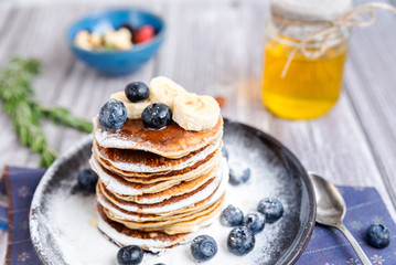 rustic Breakfast pancakes on a dark plate with blueberries and honey