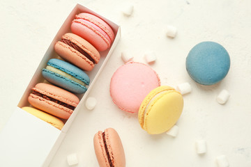 Box with different tasty macarons and marshmallows on white background