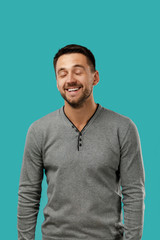 Close-up portrait of happy handsome bearded man in gray sweater laughing isolated on blue background