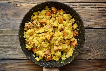 Couscous in a pan on a wooden background. Couscous with pieces of chicken in a pan.