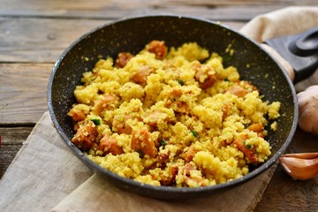 Couscous in a pan on a wooden background. Couscous with pieces of chicken in a pan.