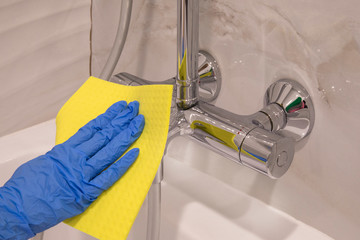Maid hand cleaning modern new basin in bathroom, water tap clean using blue gloves and yellow cloth.