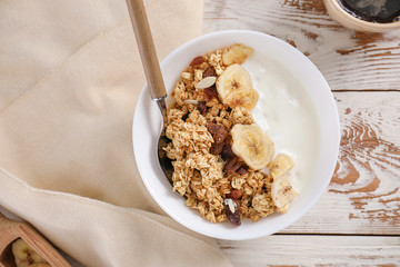 Tasty granola with yogurt in bowl on wooden table