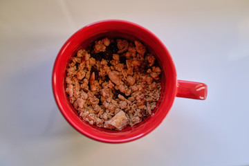 Muesli in red ceramic cup on the white table. View from top.