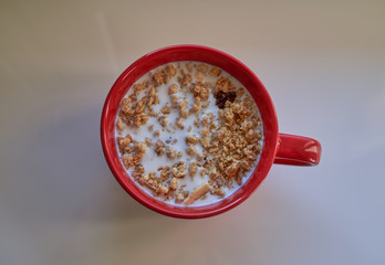 Muesli in red ceramic cup on the white table. View from top.