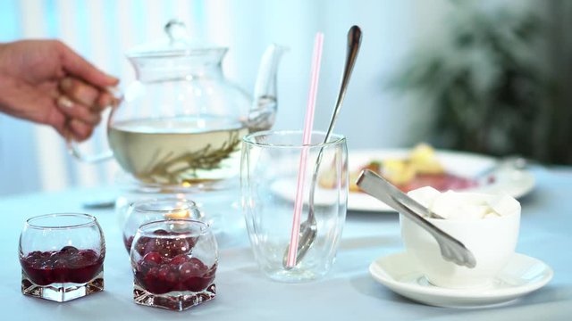 The girl&rsquo;s hand poured hot tea from a glass jar to enjoy the aroma and taste of the drink. Sugar and jam for tea additives.