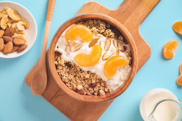 Tasty granola with yogurt in bowl on color background