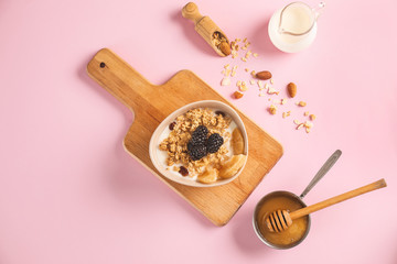 Tasty granola with yogurt in bowl on color background
