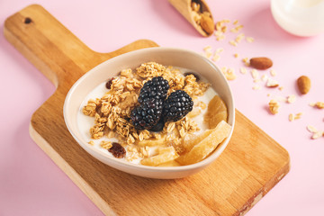 Tasty granola with yogurt in bowl on color background