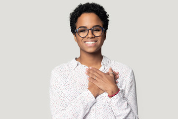 Thankful smiling black woman holding hands near heart on chest.