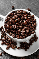 Roasted coffee beans in white cup. Dark concrete background. Top view.