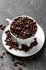 Roasted coffee beans in white cup. Dark concrete background. Top view.