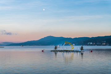 Last lights of the sunset in Velden. Reflections on the water and Christmas atmosphere. Austria.